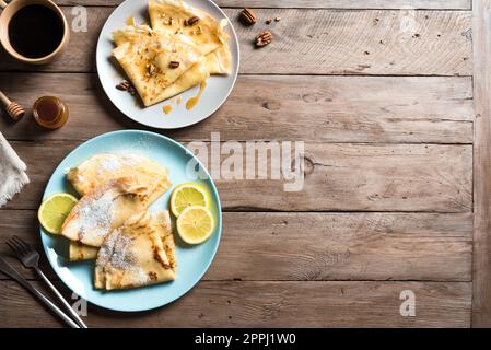 Crepes con vari condimenti - miele e noci pecan, agrumi di limone su sfondo di legno, spazio copia. Crepes fatti in casa per colazione o dessert. Foto Stock