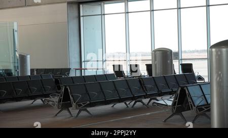 Sala terminal dell'aeroporto vuota. Posti a sedere vuoti in aeroporto - tipiche sedie nere in attesa di imbarco Foto Stock