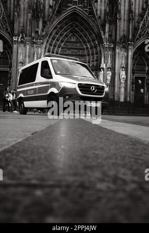 Ripresa in scala di grigi di una macchina della polizia Mercedes-Benz Sprinter di fronte alla Cattedrale di Colonia in Germania Foto Stock