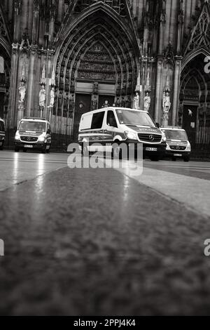 Ripresa in scala di grigi di molte auto della polizia Mercedes-Benz Sprinter di fronte alla Cattedrale di Colonia in Germania Foto Stock