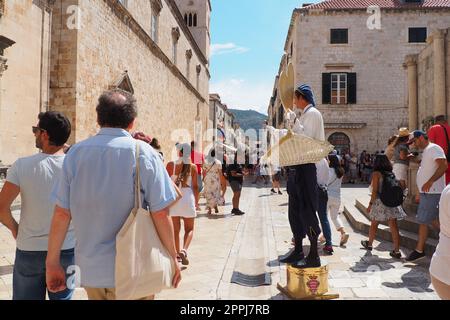 Sulle strade di Dubrovnik Croazia, felici vacanzieri camminare e comprare souvenir dal venditore nel costume nazionale festivo croato il 15 agosto 2 Foto Stock