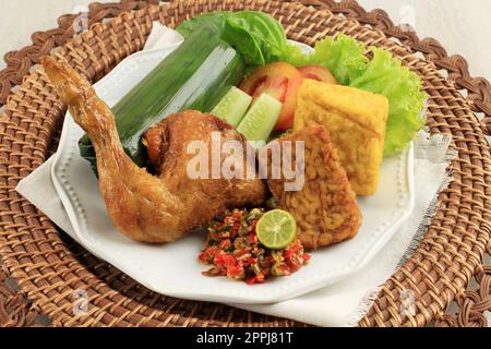 Nasi Timbel Komplit, riso tradizionale Sundanese avvolto con foglie di Banana, servito con pollo fritto, tempeh, tofu e pasta di peperoncino Foto Stock