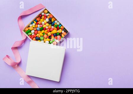 Set di caramelle dolci diverse in una scatola di carta con un nastro di raso su uno sfondo colorato. Concetto di vacanza. Foto Stock