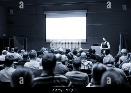 Relatore che dà un colloquio alla riunione di affari. Pubblico nella sala conferenze. Concetto di imprenditorialità e imprenditorialità. Immagine in bianco e nero con tonalità blu Foto Stock