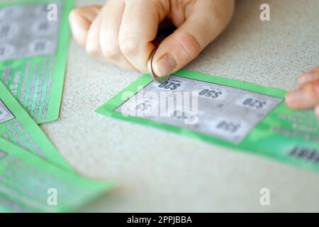 Vista ravvicinata della moneta d'argento in mano a una falsa carta della lotteria che gratta il giocatore d'azzardo. Concetto di gioco della lotteria, lotteria per graffiare le carte Foto Stock