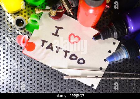 Amo il tatuaggio. Il testo è scritto su un piccolo foglio di carta tra varie attrezzature per il tatuaggio Foto Stock