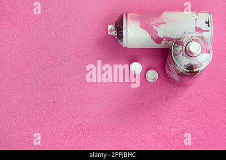 Alcune bombolette spray rosa e ugelli con gocce di vernice si trovano su una coperta di tessuto di pile rosa chiaro morbido e peloso. Colore classico del design femminile. Concetto di hooliganismo dei graffiti Foto Stock