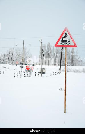 Traversata ferroviaria senza barriera con molti cartelli segnaletici nella stagione invernale innevata Foto Stock