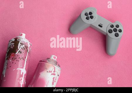 Adolescenti e concetto di stile di vita giovanile. Il joystick e due bombolette spray si trovano sulla coperta di tessuto felpato rosa peloso. Controller per videogiochi e lattine di vernice su uno sfondo in morbido pile Foto Stock