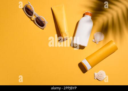 Bottiglie di crema solare e occhiali da sole su sfondo giallo, spazio copia. Vacanza estiva e cura della pelle concept, crema solare, spf uv-Protect cosmetici. Foto Stock