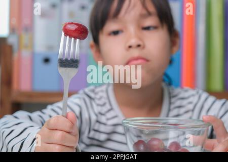 Ai bambini non piace mangiare frutta. Ragazza asiatica carina che rifiuta di mangiare frutta sana. Alimentazione e abitudini alimentari sane per i bambini. Foto Stock