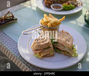 Club Sandwich con patatine fritte servite, pronto a mangiare. Sopra un tavolo di un ristorante. Foto Stock