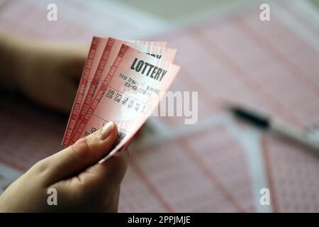 Compilare un biglietto della lotteria. Una giovane donna tiene il biglietto della lotteria con una fila completa di numeri sullo sfondo dei fogli bianchi della lotteria. Foto Stock