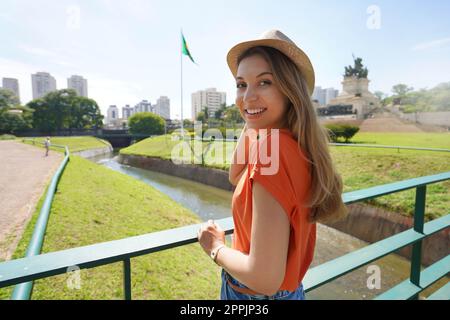 Bella ragazza che guarda la macchina fotografica con la bandiera nazionale brasiliana e San Paolo paesaggio urbano sullo sfondo, Brasile Foto Stock