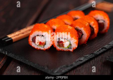 Sushi roll con gamberi e pepe rosso e tobiko caviale con insalata servita su tavola nera primo piano - cibo giapponese Foto Stock