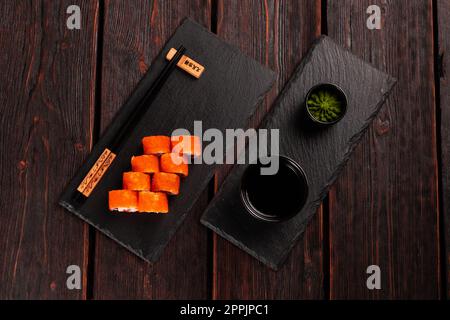 Sushi roll con gamberi e pepe rosso e caviale tobiko con insalata servita sulla lavagna nera vista dall'alto - cibo giapponese Foto Stock