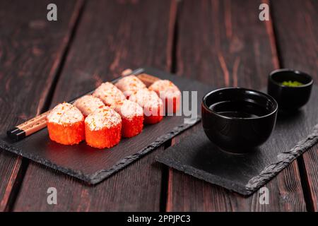 Rotolo di sushi con salsa di maionese e caviale di tobiko rosso servito su tavola nera e salsa di soia. Foto Stock