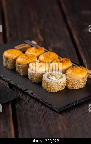 Sushi roll con anguilla, avocado e formaggio cremoso servito a bordo nero primo piano - cibo giapponese Foto Stock