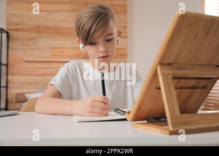 Ragazzo in auricolari che fanno i compiti a tavola al coperto Foto Stock