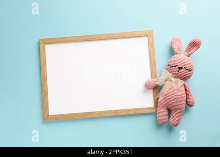 Lavagna bianca vuota con coniglietto giocattolo su sfondo turchese, piatto. Spazio per il testo Foto Stock