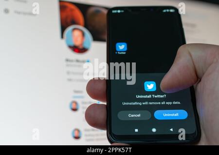 Kiev, Ucraina - 14 novembre 2022: Utente che disinstalla il social media Twitter da uno smartphone sullo sfondo del monitor con un profilo aperto di Elon Musk. Rimozione dell'app digitale a causa della dipendenza Foto Stock