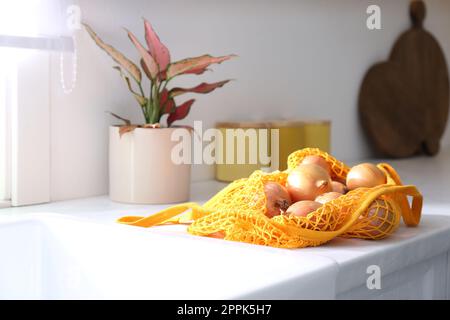 Cipolle dorate in borsa tote in rete sul banco della cucina Foto Stock