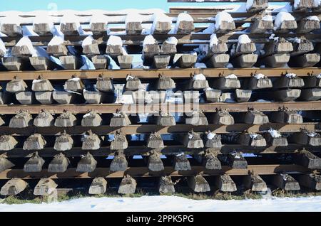 Molti vecchi binari e traversine sono impilati in un magazzino ferroviario in inverno. Il concetto di rinnovamento di una ferrovia logora Foto Stock