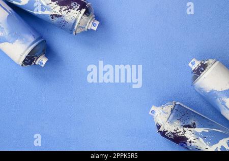 Alcune bombolette spray blu usate con gocce di vernice si trovano su una coperta di tessuto in pile blu chiaro morbido e peloso. Colore classico del design femminile. Concetto di hooliganismo dei graffiti Foto Stock