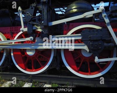 Ravvicinata delle ruote vintage di una locomotiva o di un treno. Ruote in metallo pesante grandi rosse con meccanismi di guida pistone. Locomotiva del XIX - XX secolo con motore a vapore. Foto Stock