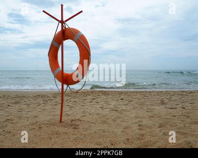 Lifebuoy su una spiaggia sabbiosa. Cerchio arancione su un palo per salvare le persone che annegano nel mare. Punto di salvataggio sulla riva. Cielo e mare sullo sfondo. Foto Stock