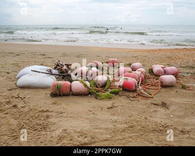 Boe nella sabbia. Una spiaggia bagnata con sabbia di quarzo grossolana. Corde aggrovigliate e boe di plastica lasciate sulla riva. Attrezzatura di sicurezza. La fine della stagione estiva. Tempo tempestoso in mare o in oceano. Bassa marea. Foto Stock