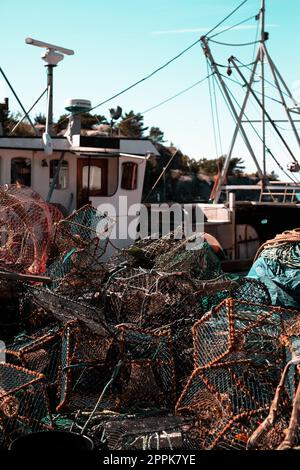 Reti da pesca impilate sul molo in un porto, primo piano rete di pescatori sfondo e barca Foto Stock