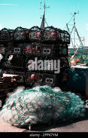 Reti da pesca impilate sul molo in un porto, primo piano rete di pescatori sfondo e barca Foto Stock