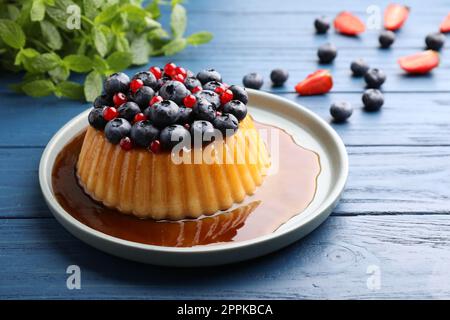 Delizioso budino con caramello e frutti di bosco su un tavolo di legno blu Foto Stock