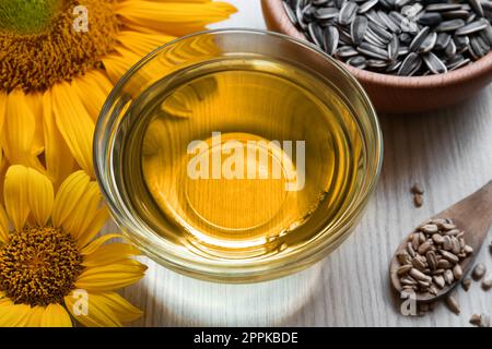 Olio di girasole in ciotola di vetro e semi su tavola di legno Foto Stock