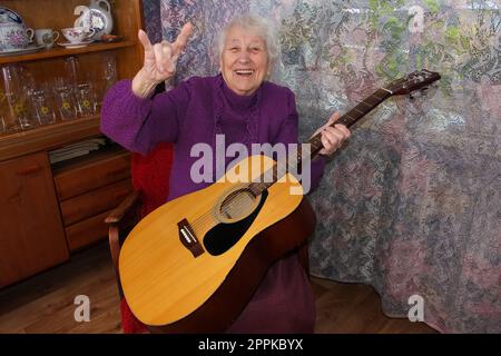 Donna anziana che suona la chitarra a casa Foto Stock