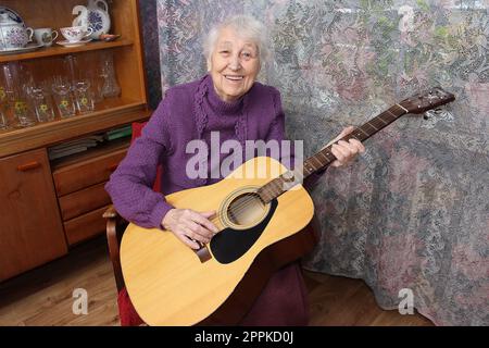 Donna anziana che suona la chitarra a casa Foto Stock