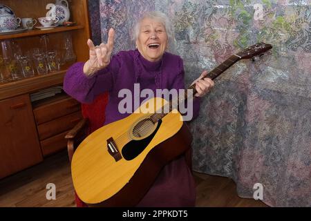 Donna anziana che suona la chitarra a casa Foto Stock