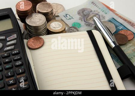 Pile di monete e banconote con calcolatrice, taccuino e penna Foto Stock