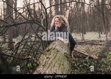 Donna dai capelli ricci che riposa sulla fotografia panoramica del tronco dell'albero Foto Stock