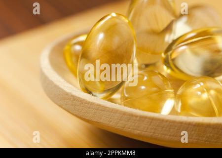 Capsule di gel morbido di olio giallo su fondo di legno. Capsula per pillola cosmetica di vitamina e, A, olio di mandorle, Omega 3, pesce. Foto Stock
