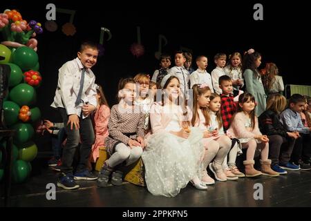 Sremska Mitrovica, Serbia 8 marzo 2022 spettacolo di coro per bambini sul palco. I bambini cantano. Gruppo musicale per bambini in eleganti costumi eseguono canzoni natalizie per le madri. Scena oscura. Foto Stock