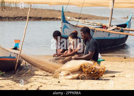 Pescatore e donna che riparano reti da pesca agli estuari di un fiume. La donna ha un volto dipinto tradizionalmente malgascio Foto Stock