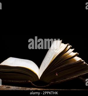 Vecchio libro aperto su un tavolo vintage su sfondo scuro. Foto Stock