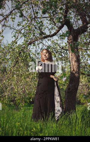 Donna in vestito nero sotto l'albero abbracciando se stessa fotografia panoramica Foto Stock