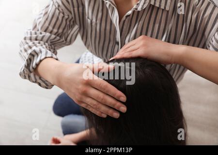 Madre che esamina i capelli di sua figlia in casa. Trattamento antighiaccio Foto Stock