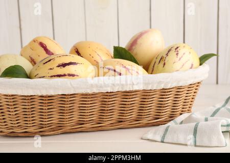 Meloni di pepino freschi maturi con foglie verdi in cestino di vimini su tavolo di legno bianco Foto Stock