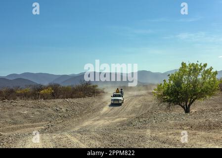 Auto su una strada di ghiaia polverosa lungo il fiume Kunene nel nord della Namibia Foto Stock