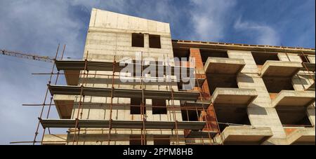 Costruzione di un quarto di case a cinque piani in cemento monolitico. Industria, edilizia, immobiliare. Facciata dell'edificio, ponteggi. Nuove tecnologie di costruzione per le aree soggette a sismici. Foto Stock