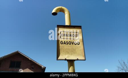 Cartello gas con iscrizioni in serbo, montenegrino e croato - attenzione gas. Cartello metallico schiacciato su sfondo blu. Gasdotto che attraversa la campagna. Serbia, Sremska Mitrovica Foto Stock